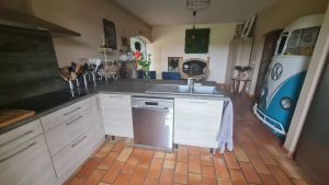 Cuisine meublée et équipée ouverte sur la salle à manger, avec l’avant d’un combi Volkswagen vintage intégré en élément décoratif