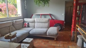 Tranche authentique de Mini Austin intégrée dans un salon cosy, avec cabine téléphonique rouge, pour une ambiance typiquement anglaise