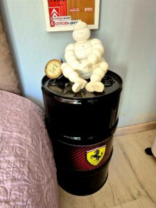 Table de nuit réalisée avec un fût portant le logo Ferrari, surmontée d’une lampe Bibendum Michelin, déco chambre Pole Position