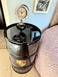 Fût noir avec logo Porsche utilisé comme table de nuit, surmonté d'une horloge en forme de phare de voiture, déco originale chambre Pole Position